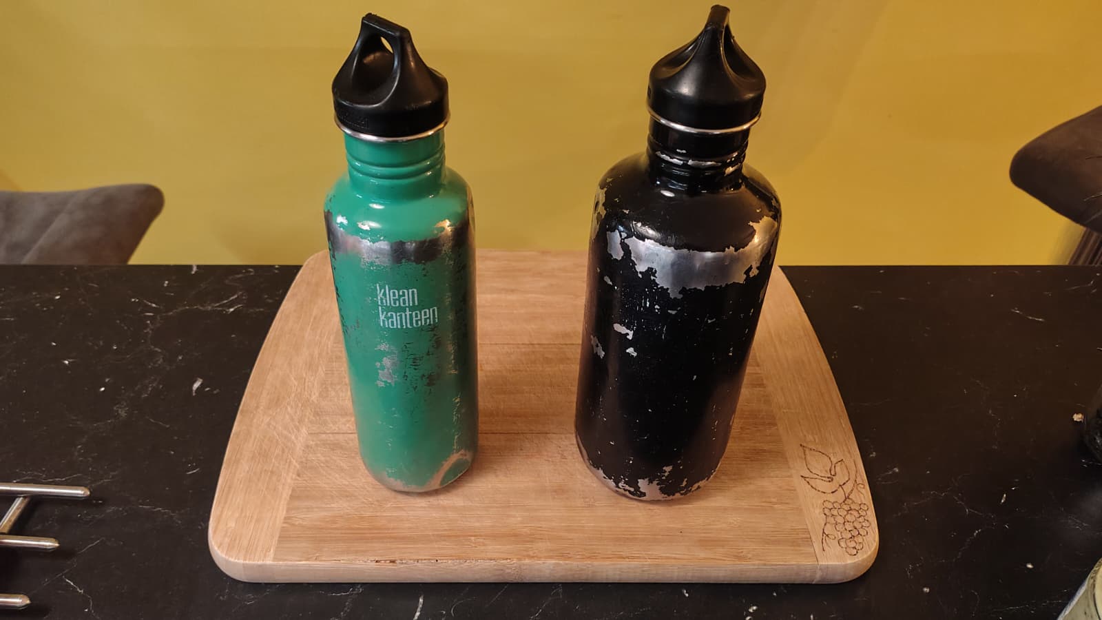 Unsere grüne und schwarze Edelstahlflasche mit deutlich sichtbaren Lackabplatzungen auf einem Holzbrett